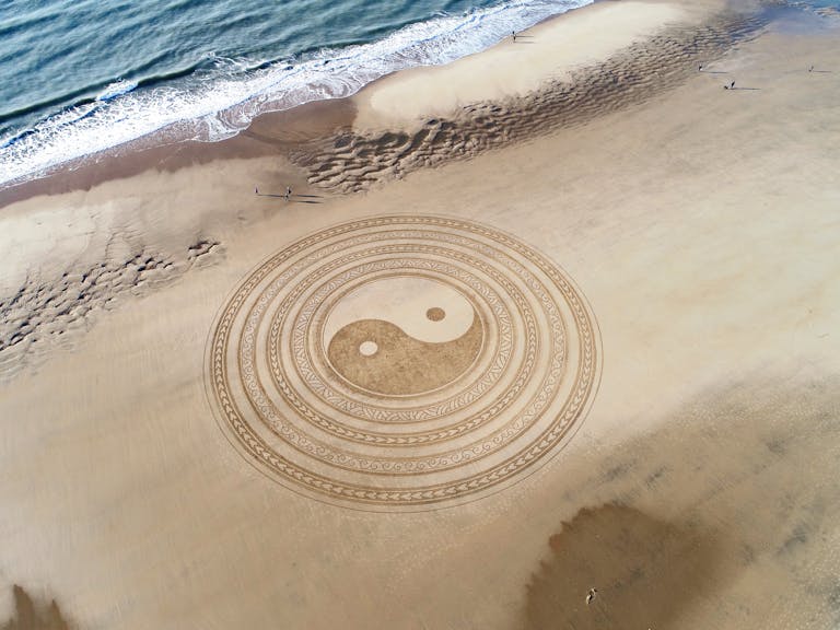 Yin Yang symbol drawn on brown beach sand, symbolizing balance, harmony, and the unity of opposites in a natural setting.